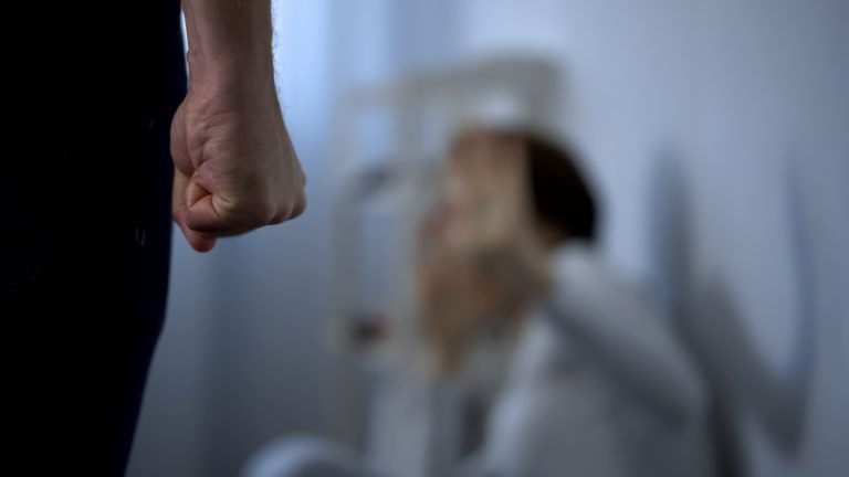 Violência contra a mulher - homem com punho cerrado indo ao encontro de uma mulher encolhida no chão