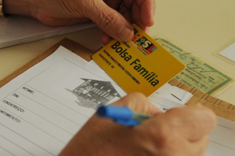 Uma pessoa segura um cartão do Bolsa Família e preenche um formulário