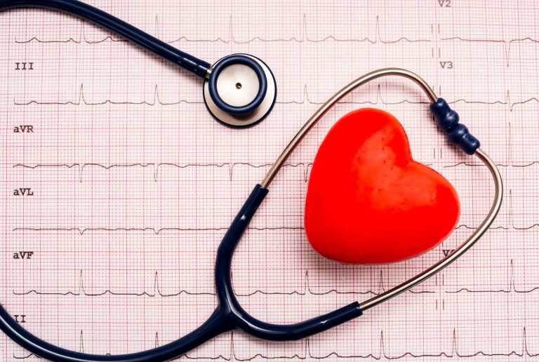 Estetoscópio e bolinha de massagem em formato de coração em cima de um eletrocardiograma