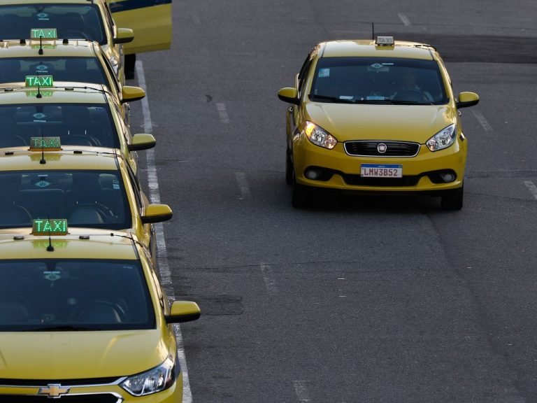 Fila de táxis estacionados e um táxi passando ao lado, todos os carros são amarelos - Rio de Janeiro
